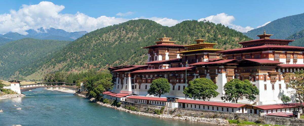 A traditional multi-tiered building with a river in the foreground and mountains in the background.