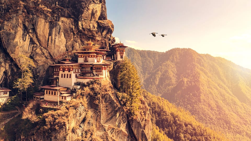 A monastery perched on a cliffside with a mountainous backdrop.