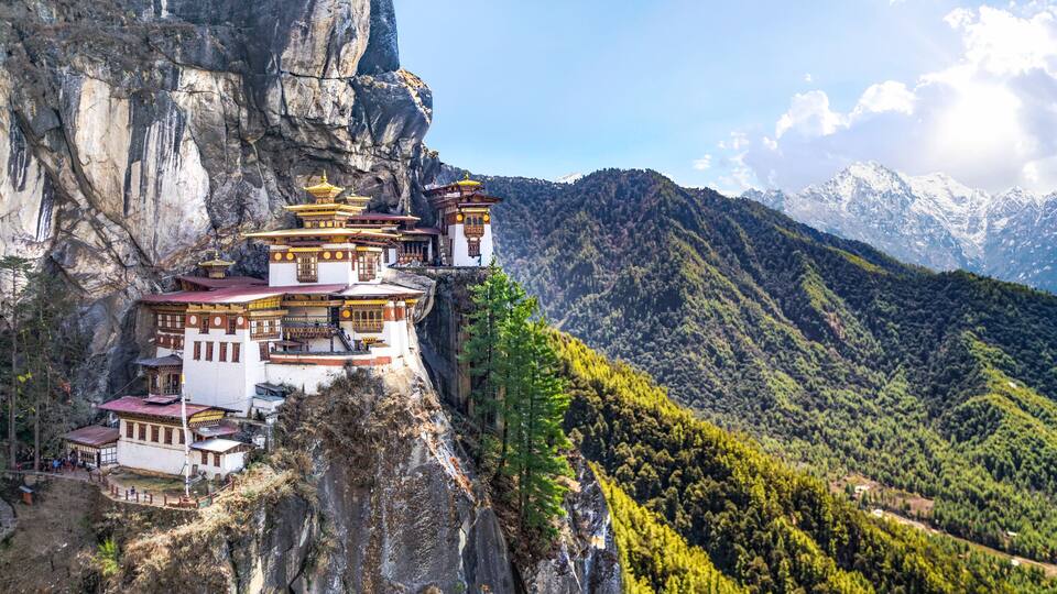 A monastery perched on a cliffside with a mountainous backdrop.