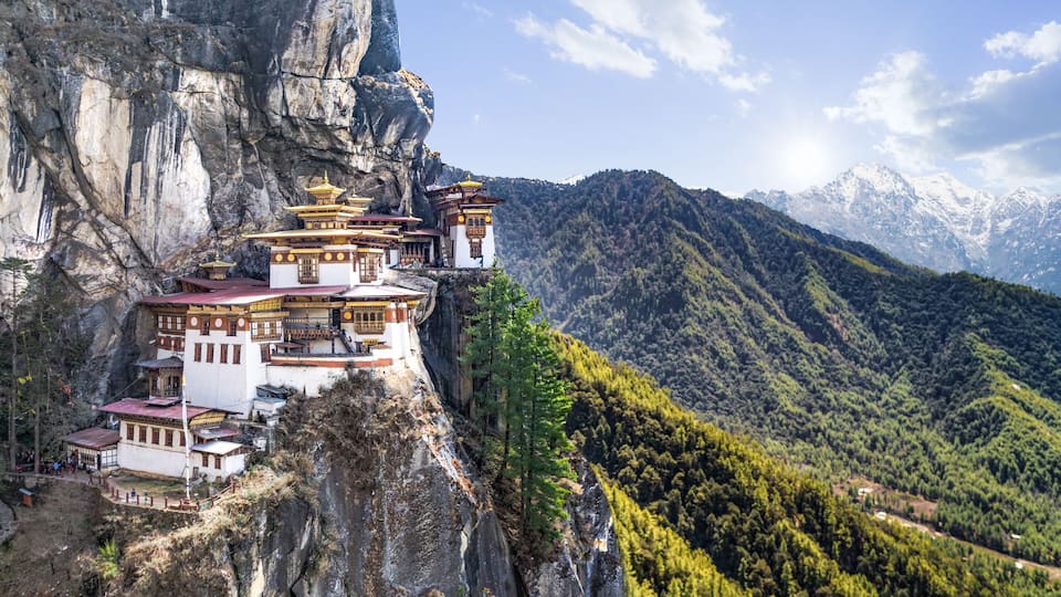 A monastery perched on a cliffside with a mountainous backdrop.
