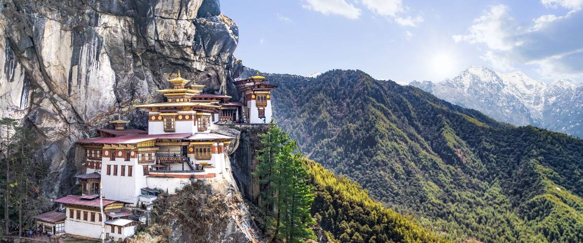 A monastery perched on a cliffside with a mountainous backdrop.