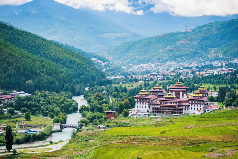 A mountainous landscape with terraced fields, a river, and a large monastery with multiple buildings.