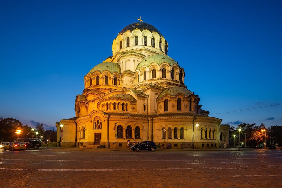 A large, ornate church with multiple domes and arched windows, illuminated at dusk.