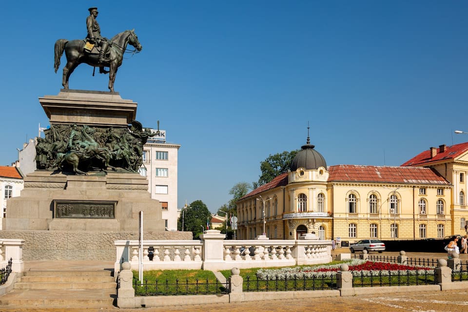 A statue of a man on a horse, a fountain, and a building with a red roof.
