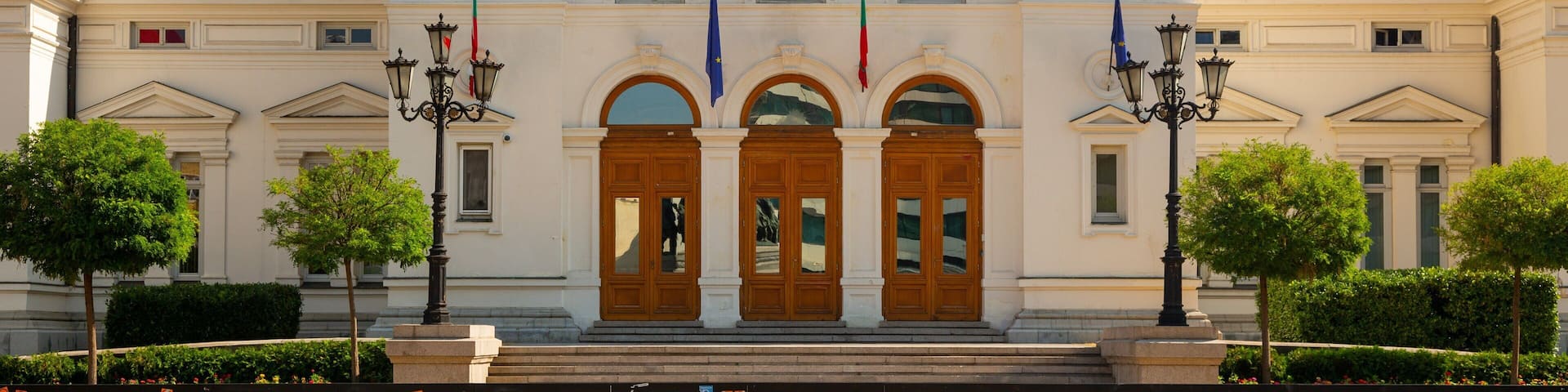 A grand building with a large emblem above the entrance, flags, and ornate lamp posts.