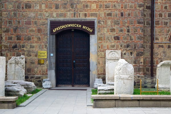 A stone building with a large arched entrance and a sign reading "Arxeologicheski Museum".