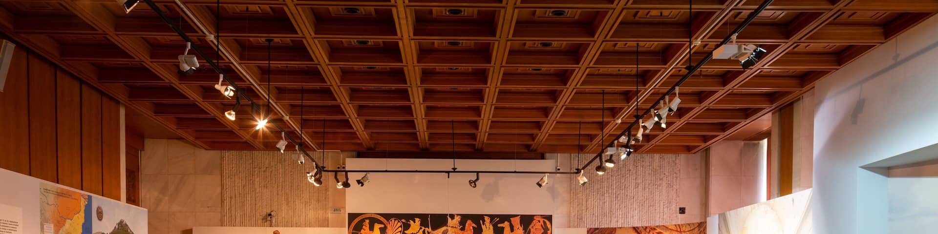 Un museo en el interior con vitrinas de vidrio que exhiben artefactos, vigas de madera en el techo y carteles informativos en las paredes.