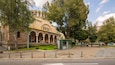 A historic church with arched windows and a green dome, surrounded by trees and a bus stop.