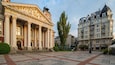 Un magnifique théâtre aux colonnes et statues classiques, entouré d’une place dallée de motifs géométriques et bordé de bâtiments modernes.