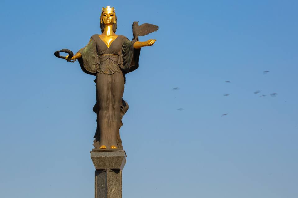 Una estatua de una mujer con un pájaro en el hombro, llevando una corona y sosteniendo un báculo.