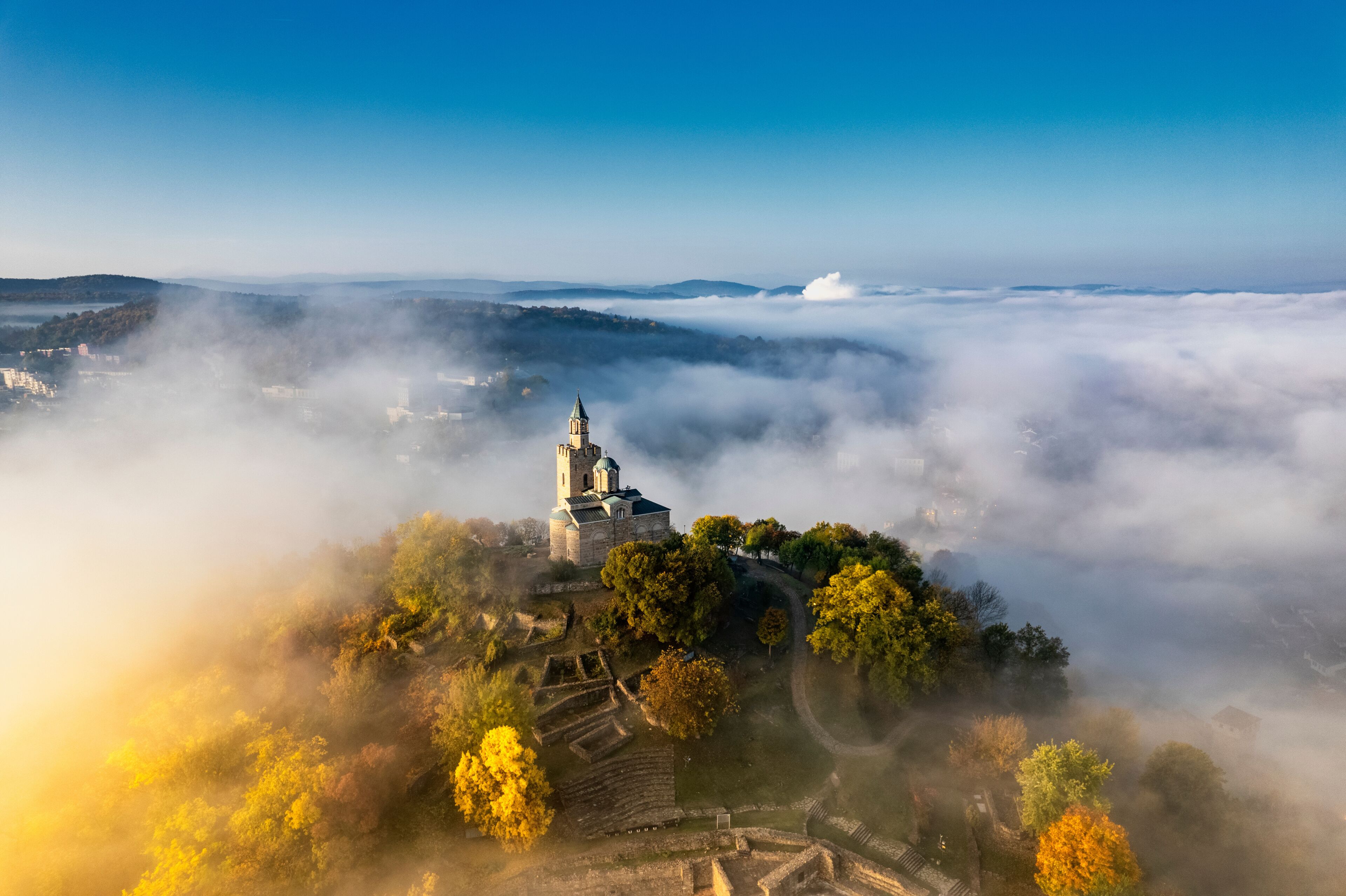 A church on a hill surrounded by autumn foliage and mist.
