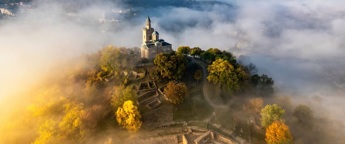 A church on a hill surrounded by autumn foliage and mist.