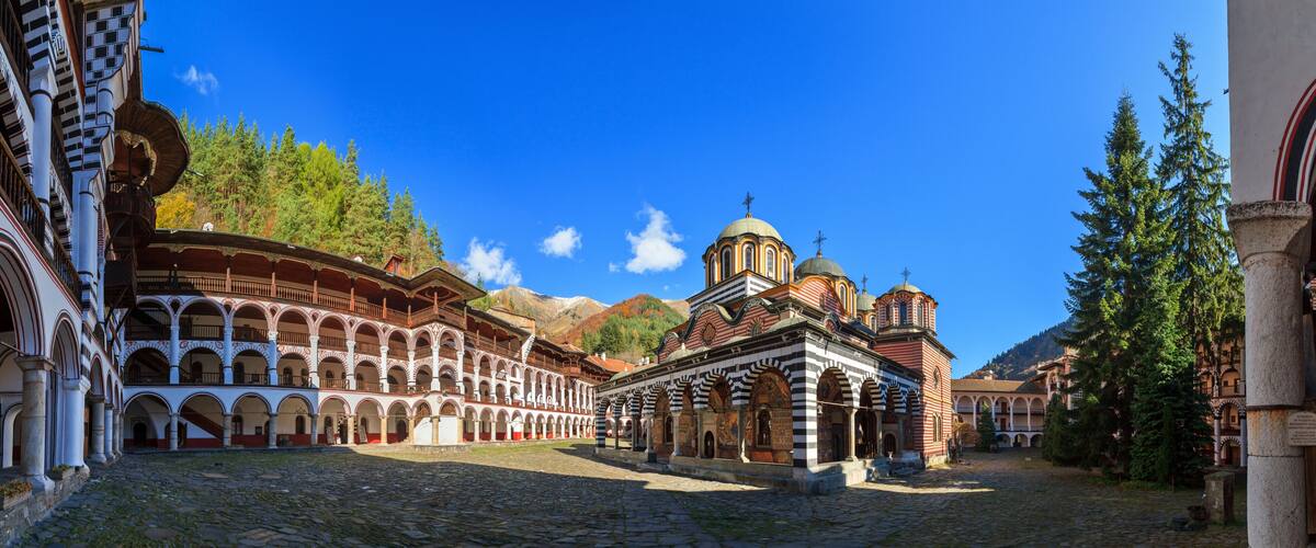 A historic courtyard with a church featuring domed architecture and a stone building with arched walkways.