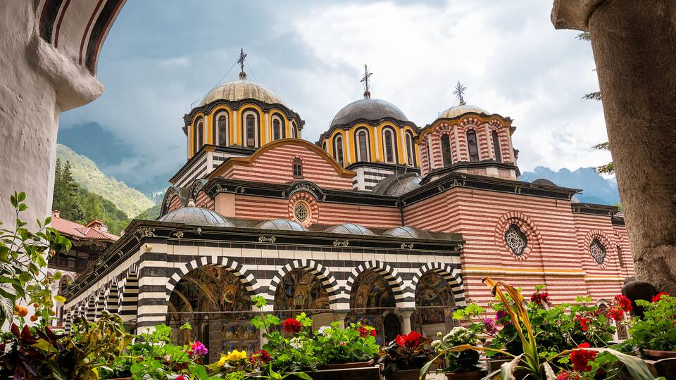 A historic church with multiple domes and striped architecture, surrounded by lush greenery and potted plants.