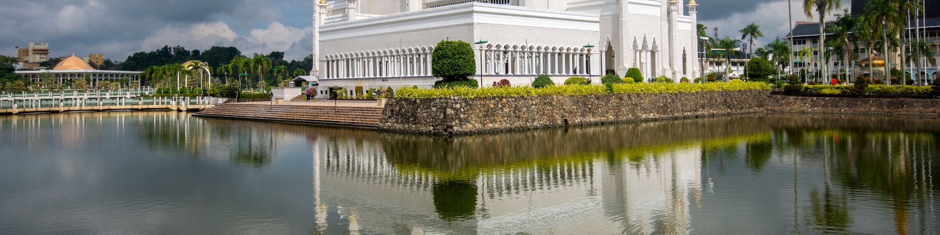 Uma grande mesquita branca com uma cúpula dourada e várias minaretes, refletindo em águas calmas.