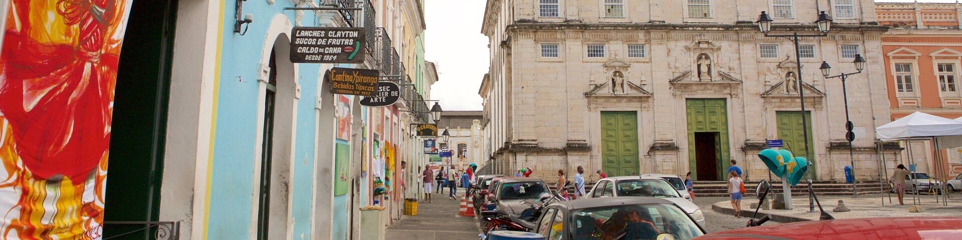 A colorful street with a sign for Pau Brasilis, a historic building with a cross on top, and parked cars.