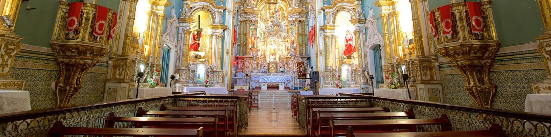 Interior ornamentado de iglesia con detalles dorados, banderines rojos y un altar central.