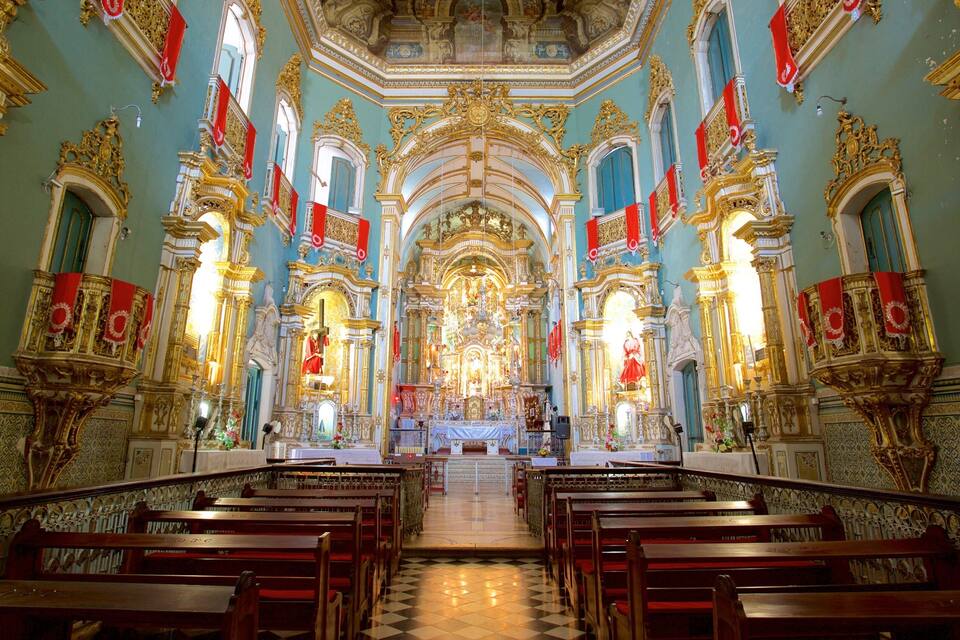 Interno di una chiesa decorata con ornamenti dorati, stendardi rossi e un altare centrale.