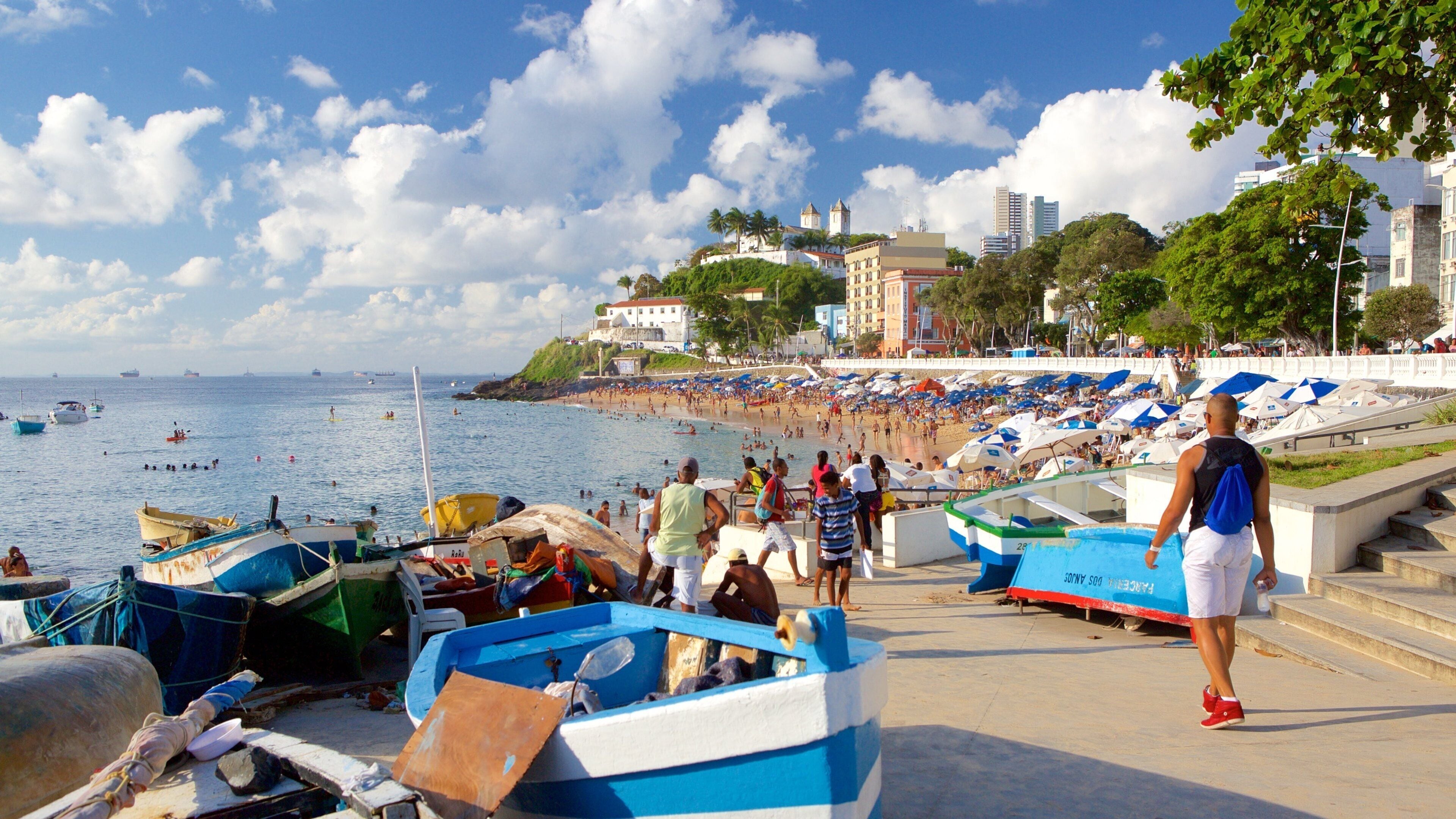 Une plage bondée, avec des gens, des bateaux et des bâtiments en arrière-plan.