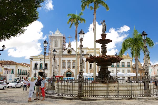 Une place historique dotée d’une fontaine centrale, de palmiers et de bâtiments à l’architecture riche et élaborée.