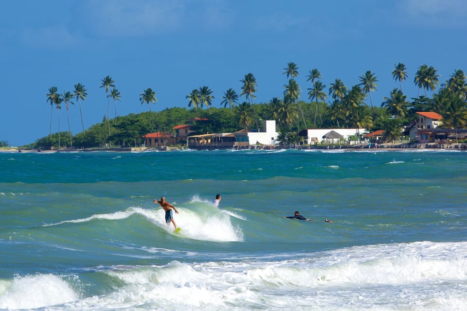 A beach with surfers, palm trees, and coastal buildings.