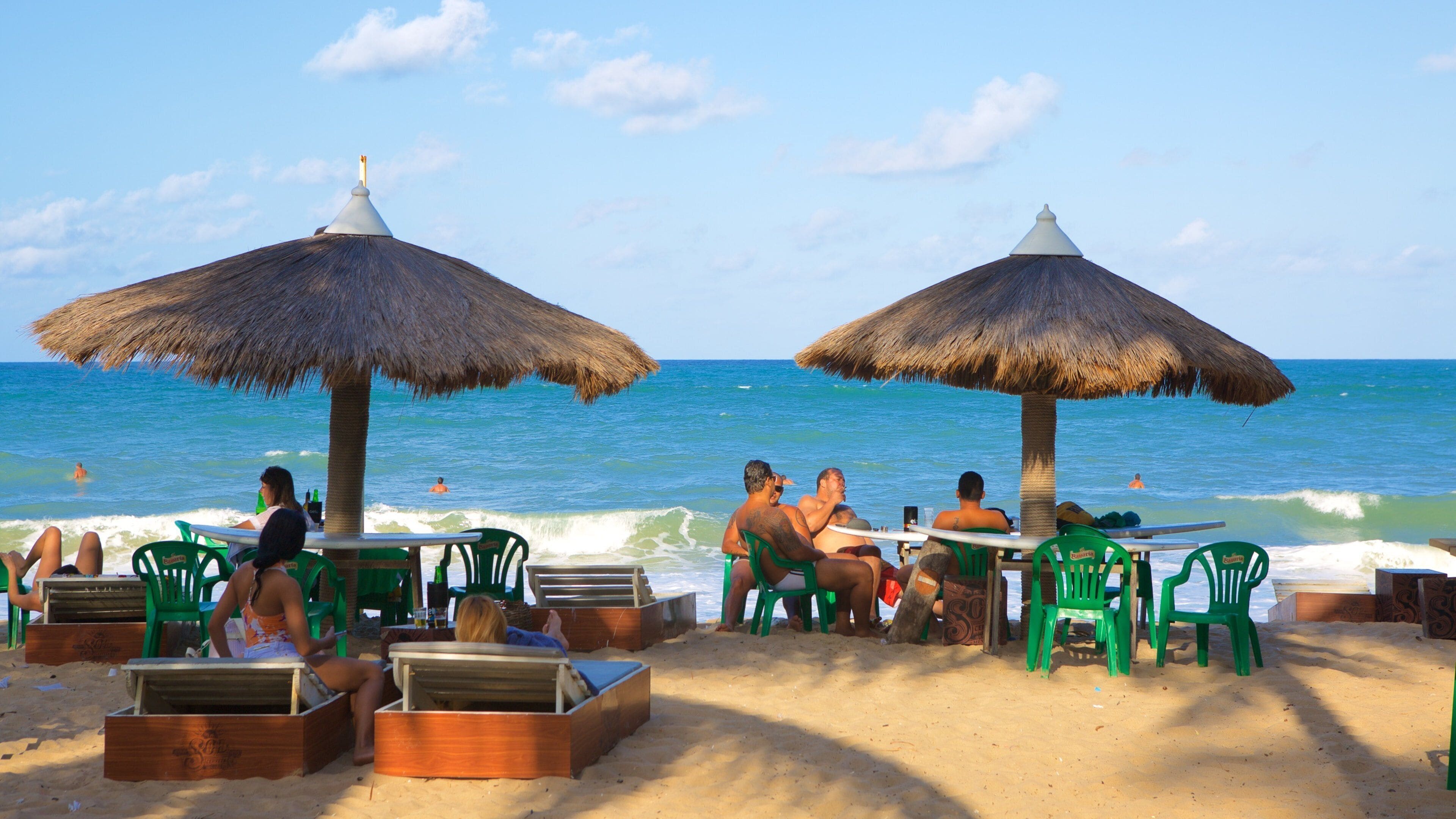 A beach with thatched umbrellas, lounge chairs, and people relaxing by the ocean.
