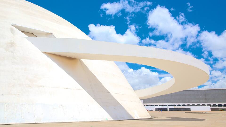 A modern architectural structure with a curved white facade and a clear blue sky with clouds.