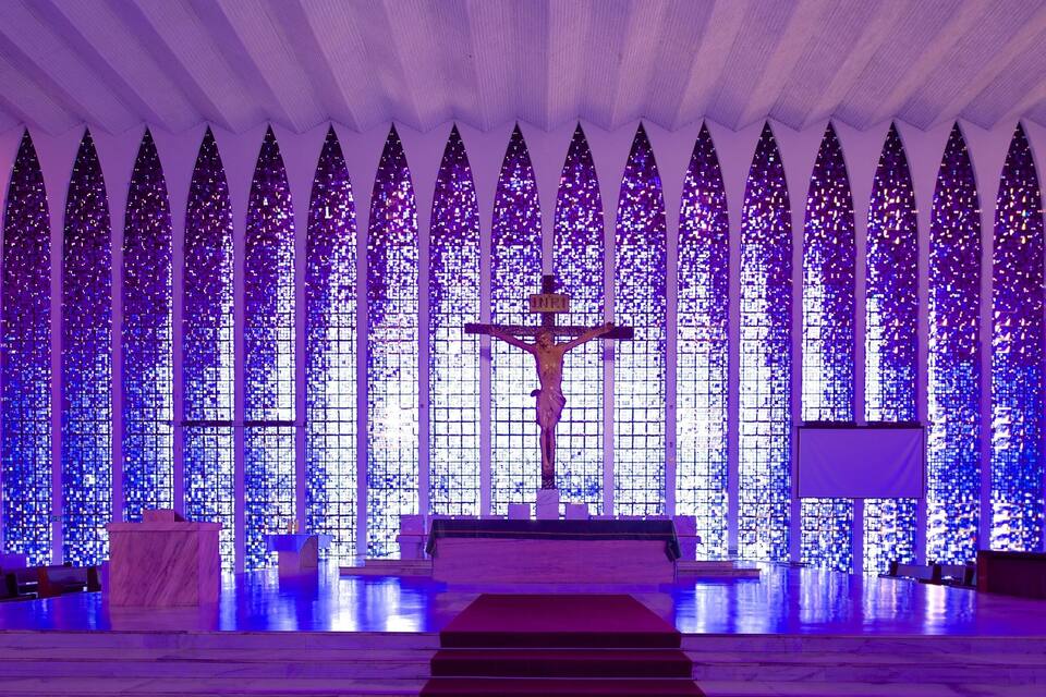 Interior de igreja com um crucifixo no altar, vitrais e bancos.