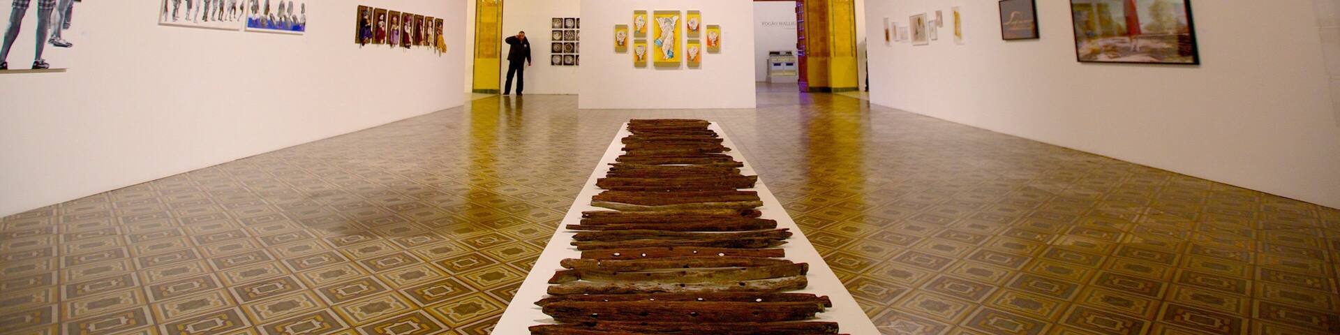An art gallery with a central installation of wooden planks and a large spherical sculpture.
