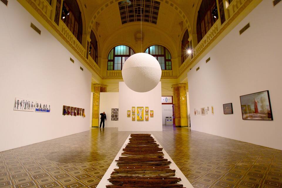 Een kunstgalerie met een centraal kunstwerk bestaande uit houten planken en een grote bolvormige sculptuur.