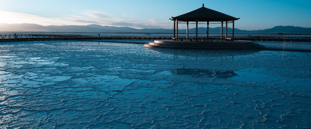 A gazebo on a frozen lake with mountains in the background.