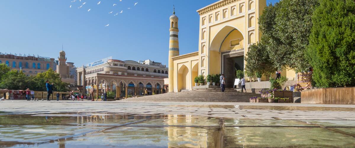A historic building with an archway and a minaret, surrounded by a reflective water surface and greenery.