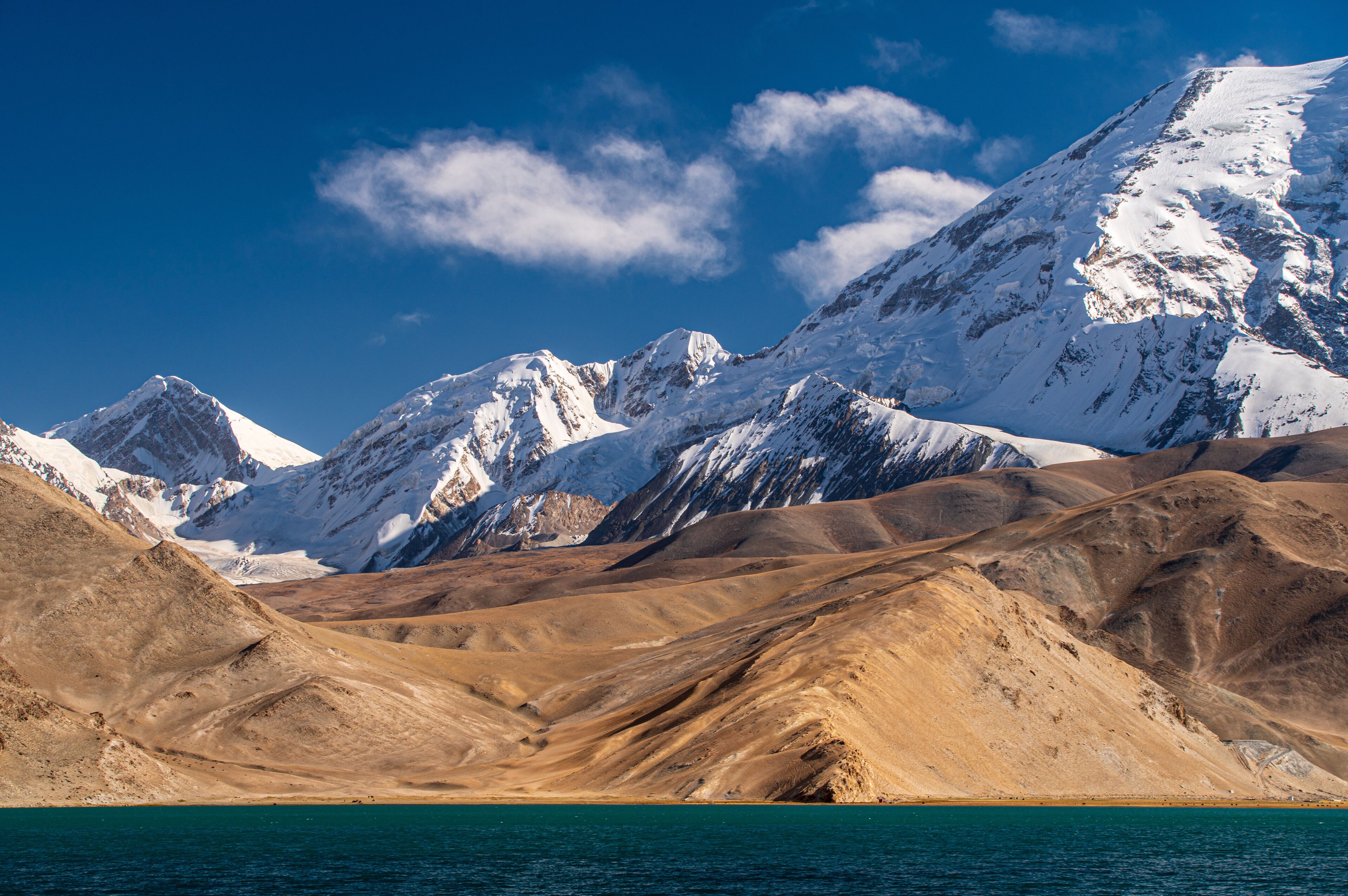Snow-capped mountains, a desert landscape, and a turquoise lake.