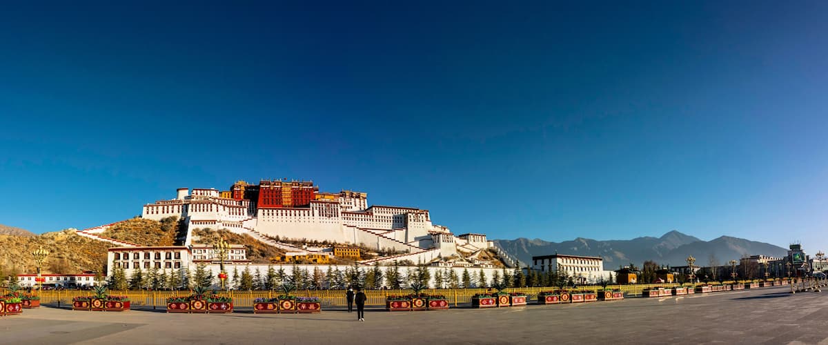 A large fortress-like structure with multiple levels and a flat top, surrounded by a well-maintained garden and a clear blue sky.