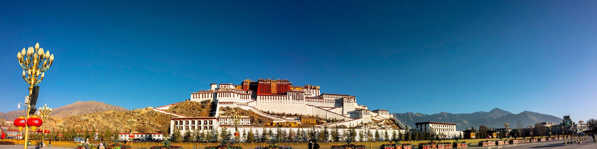 A large fortress-like structure with multiple levels and a flat top, surrounded by a well-maintained garden and a clear blue sky.