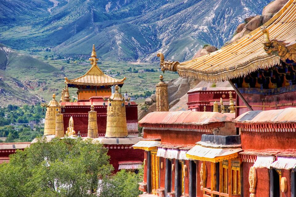 Un monasterio tibetano tradicional con arquitectura ornamentada, frente a un paisaje montañoso.