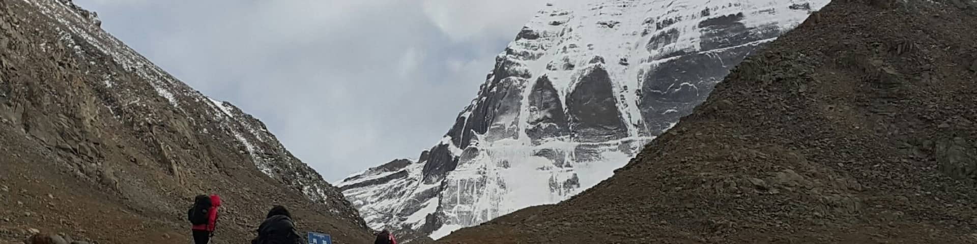 A rocky mountain path with hikers and a snow-capped peak in the background.