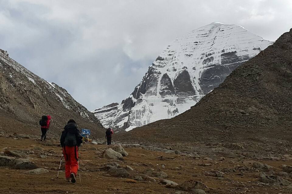 A rocky mountain path with hikers and a snow-capped peak in the background.