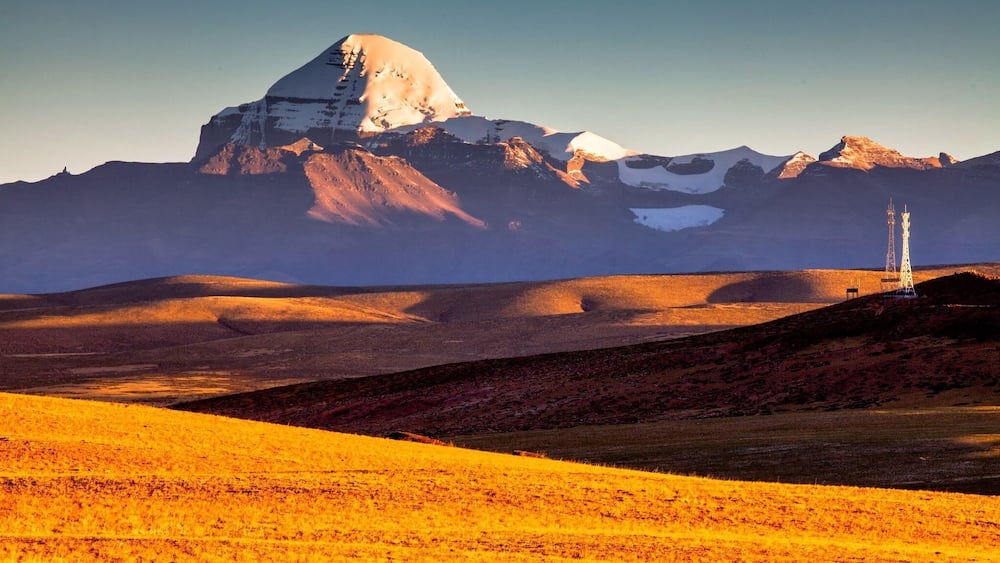 A mountain landscape with a prominent peak, rolling hills, and two communication towers.