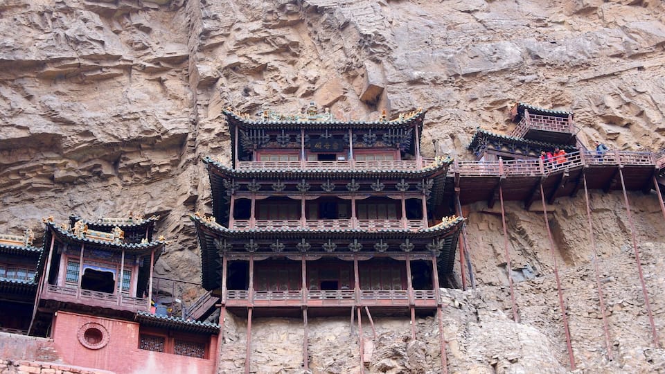 A traditional multi-tiered building with ornate roofs, constructed against a rocky cliff face.