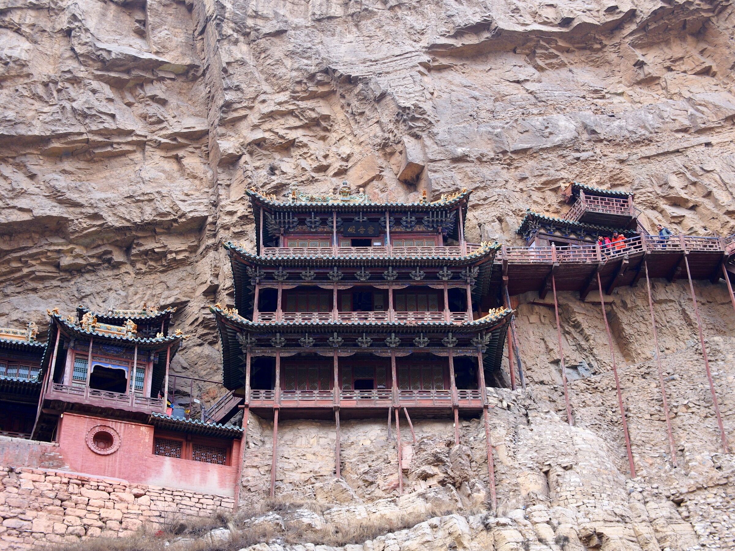 A traditional multi-tiered building with ornate roofs, constructed against a rocky cliff face.