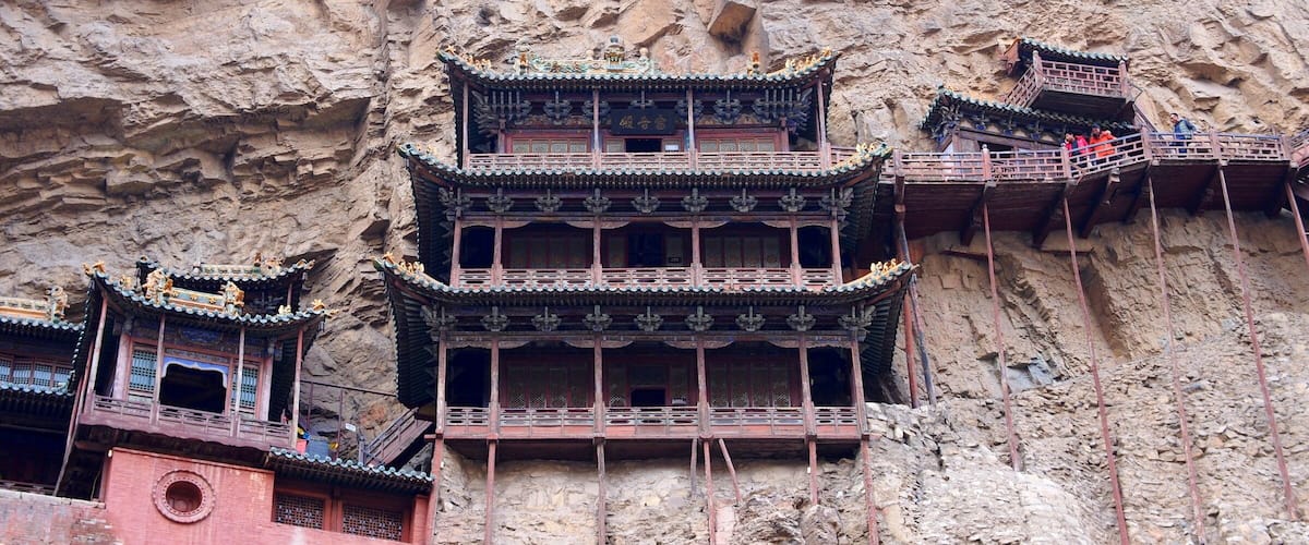 A traditional multi-tiered building with ornate roofs, constructed against a rocky cliff face.