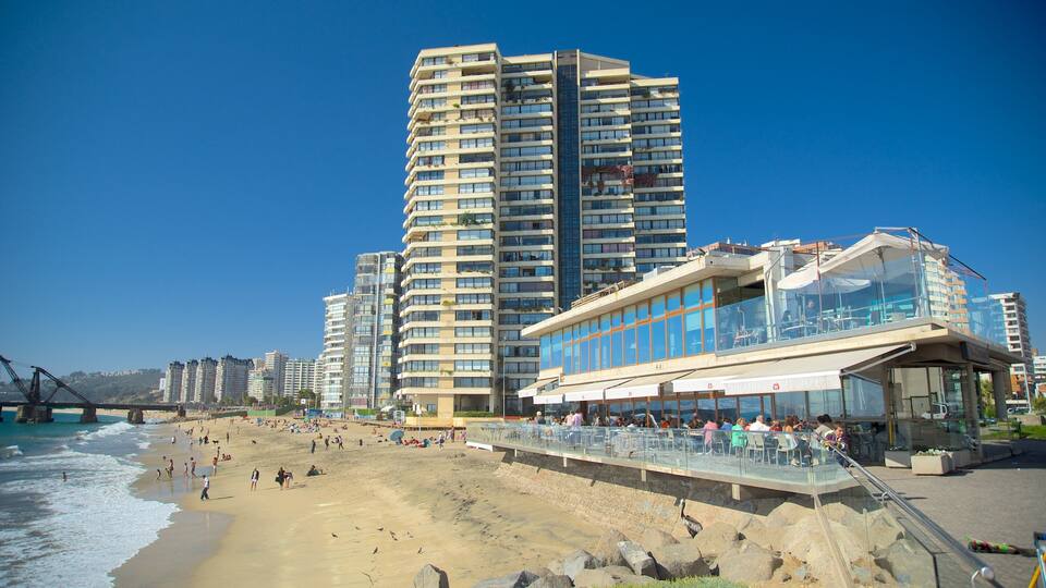 A beach with high-rise buildings, a glass-walled restaurant, and a rocky shoreline.