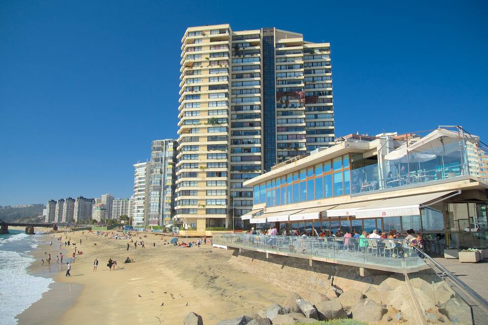 Una playa con rascacielos, un restaurante de paredes de vidrio y un litoral rocoso.