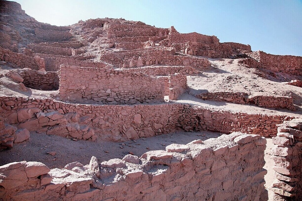 Ancient stone ruins with stepped terraces and walls in a desert landscape.