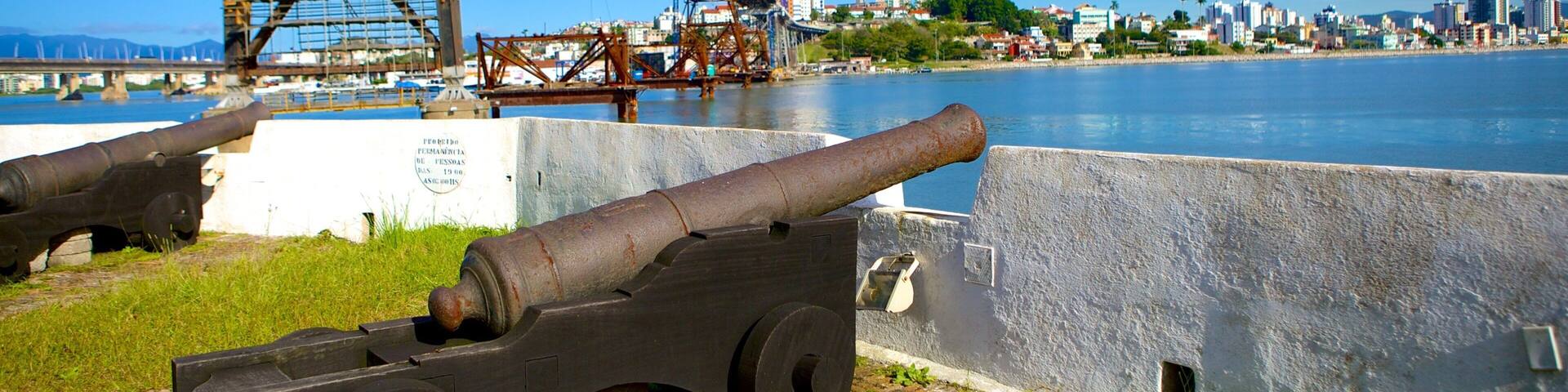 A cannon, a bridge, and a cityscape across a river.