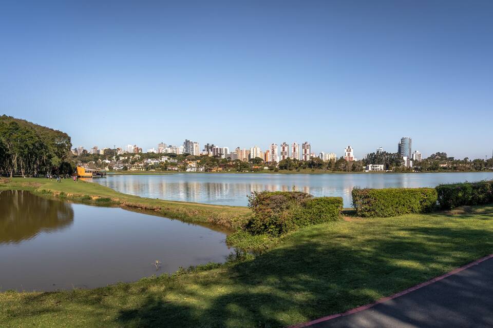 A park with a pond, a walking path, and a city skyline in the background.