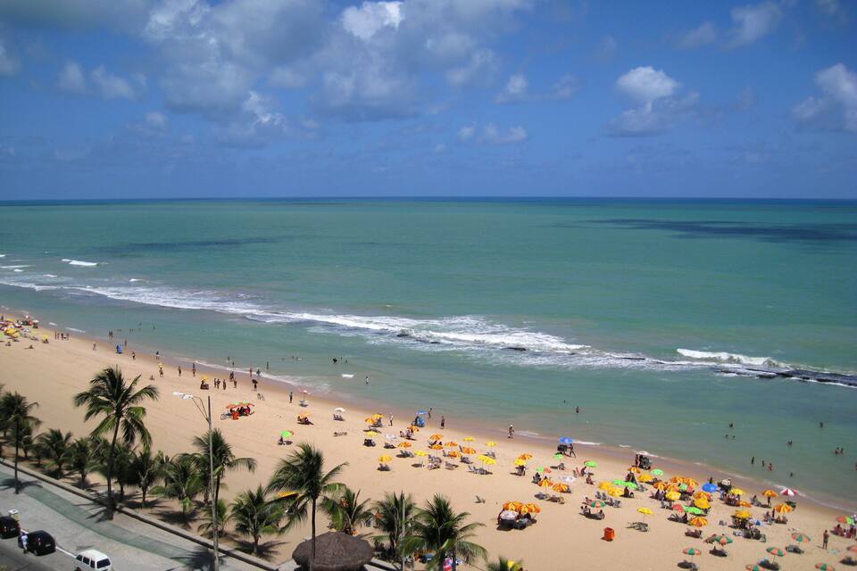 A beach with palm trees, umbrellas, and people.