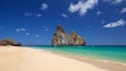 A beach with clear turquoise waters, a large rock formation, and a sandy shore.