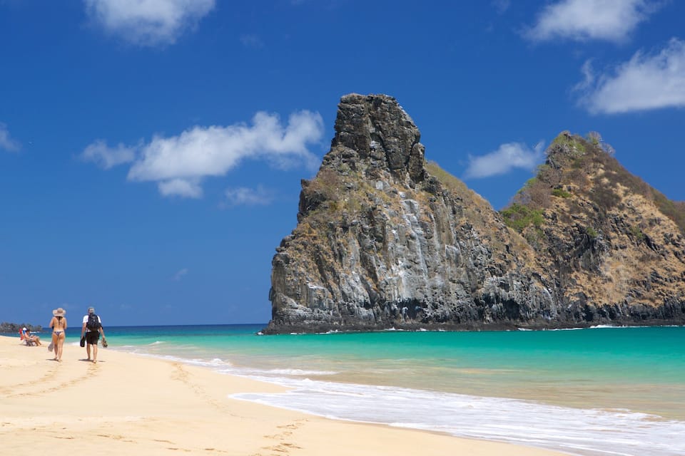 A beach with clear turquoise waters and rocky cliffs.